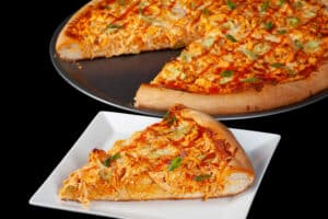 A buffalo chicken pizza with shredded chicken, celery, red onion, Monterey Jack cheese, hot sauce, and ranch dressing.