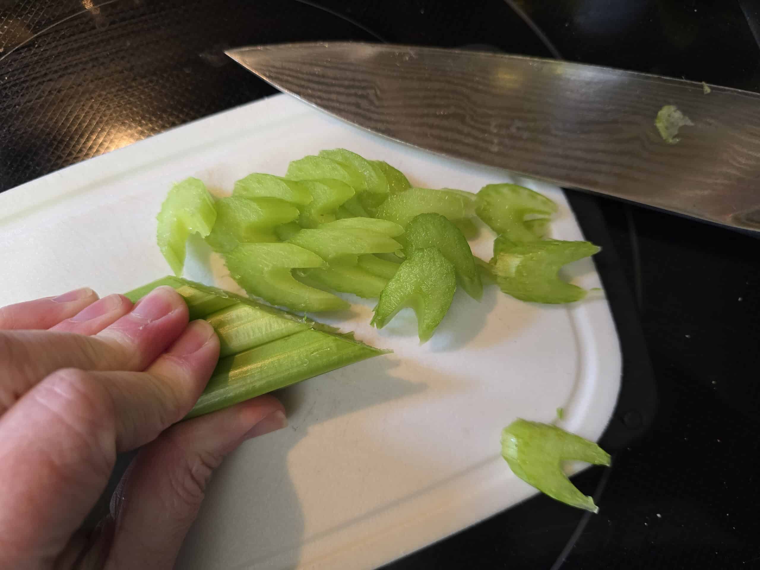 A hand cutting celery ribs on the diagonal, making shapes that look like star trek insignias.