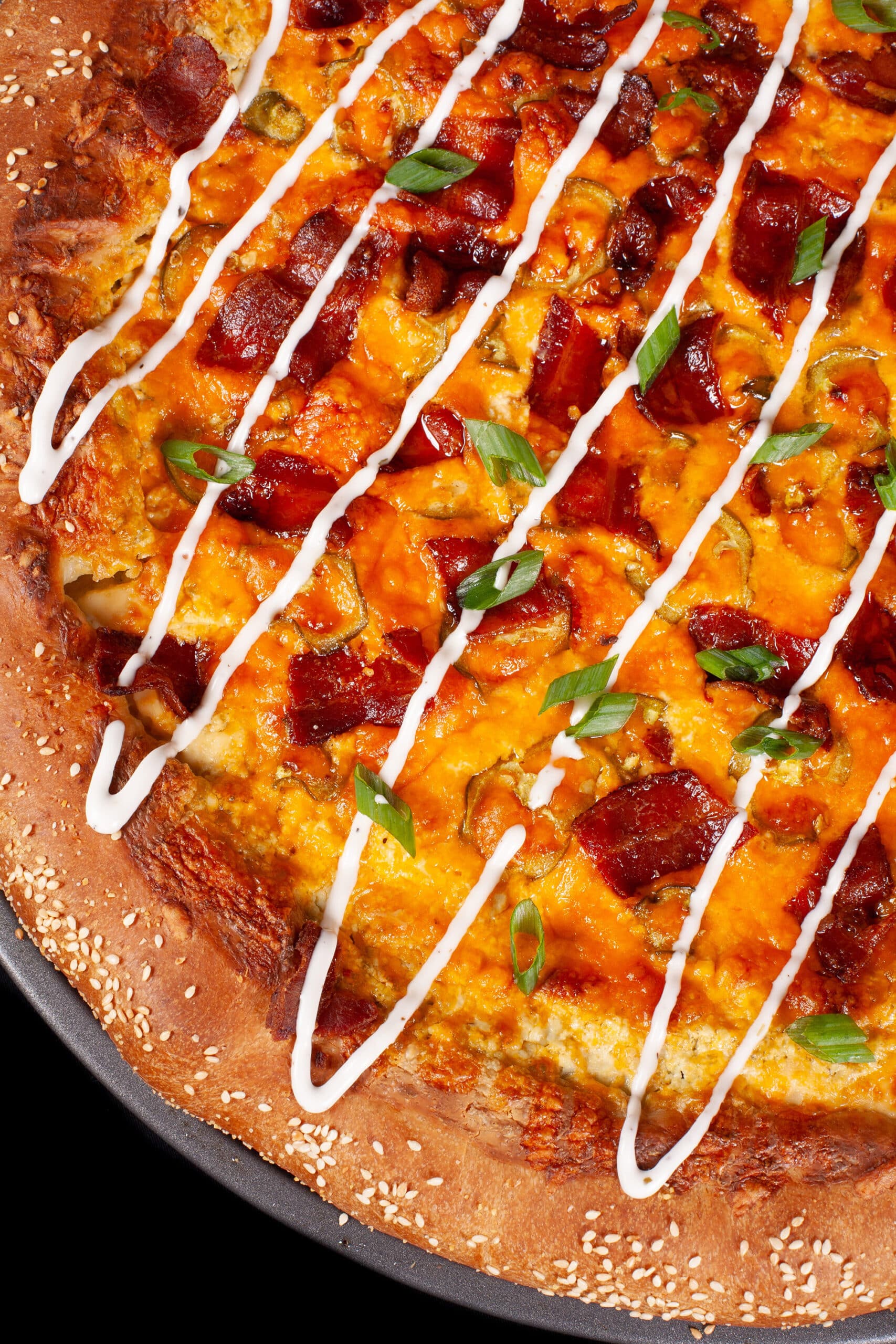 A bacon jalapeno popper stuffed crust pizza drizzled with ranch dressing and topped with sliced green onions.