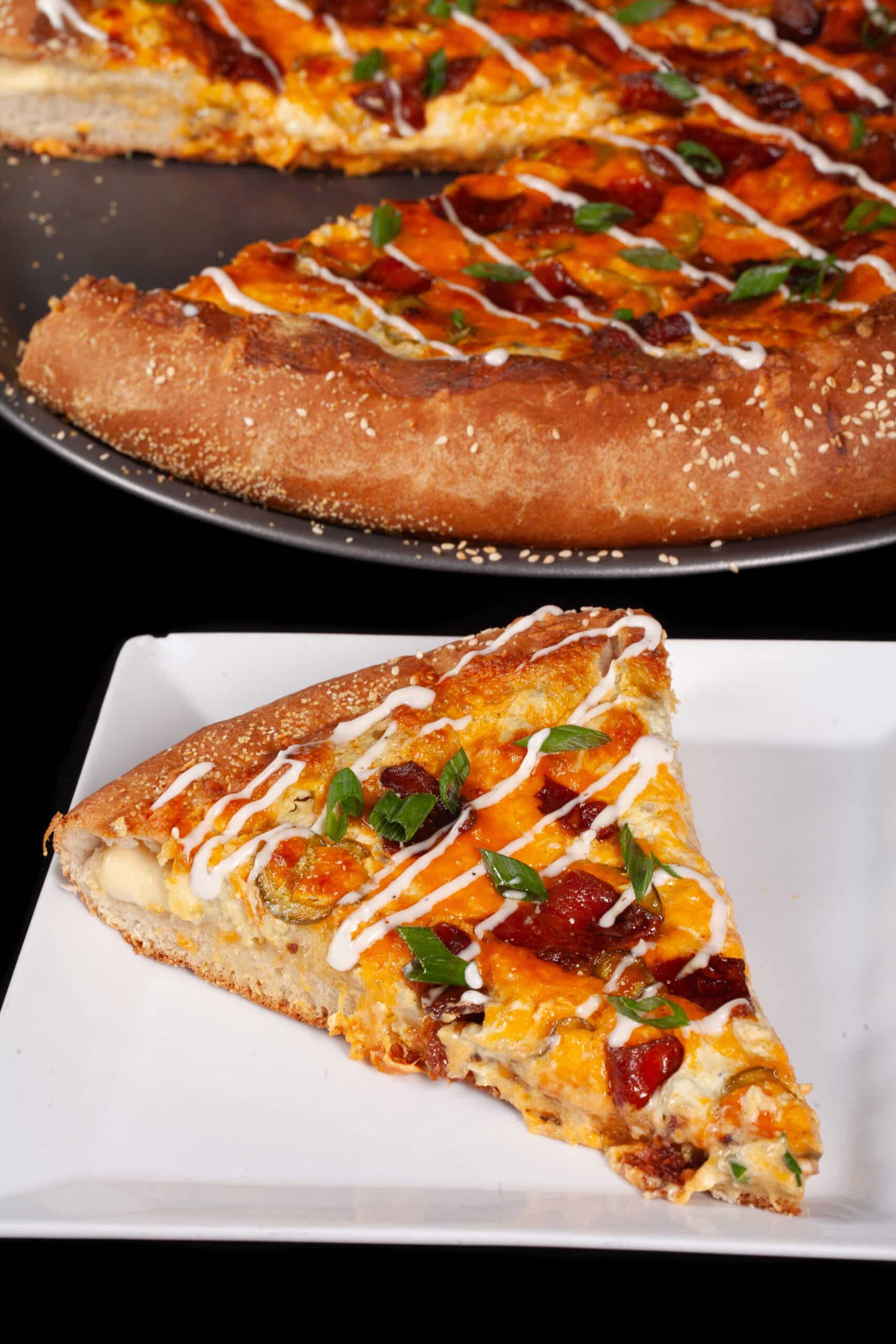 A stuffed crust bacon jalapeno popper pizza drizzled with ranch dressing and topped with sliced green onions.