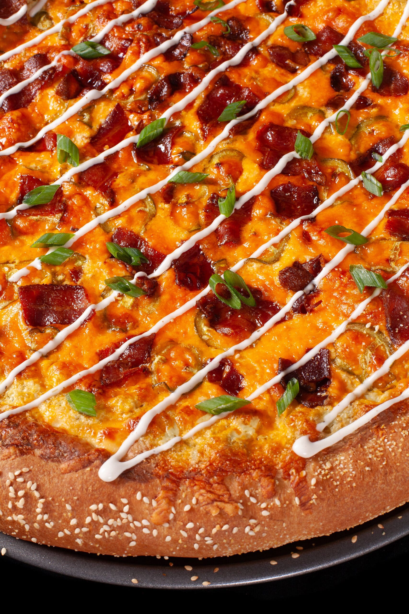 A bacon jalapeno popper stuffed crust pizza drizzled with ranch dressing and topped with sliced green onions.