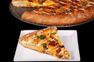 A stuffed crust bacon jalapeno popper pizza drizzled with ranch dressing and topped with sliced green onions.