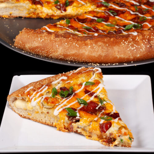 A stuffed crust bacon jalapeno popper pizza drizzled with ranch dressing and topped with sliced green onions.