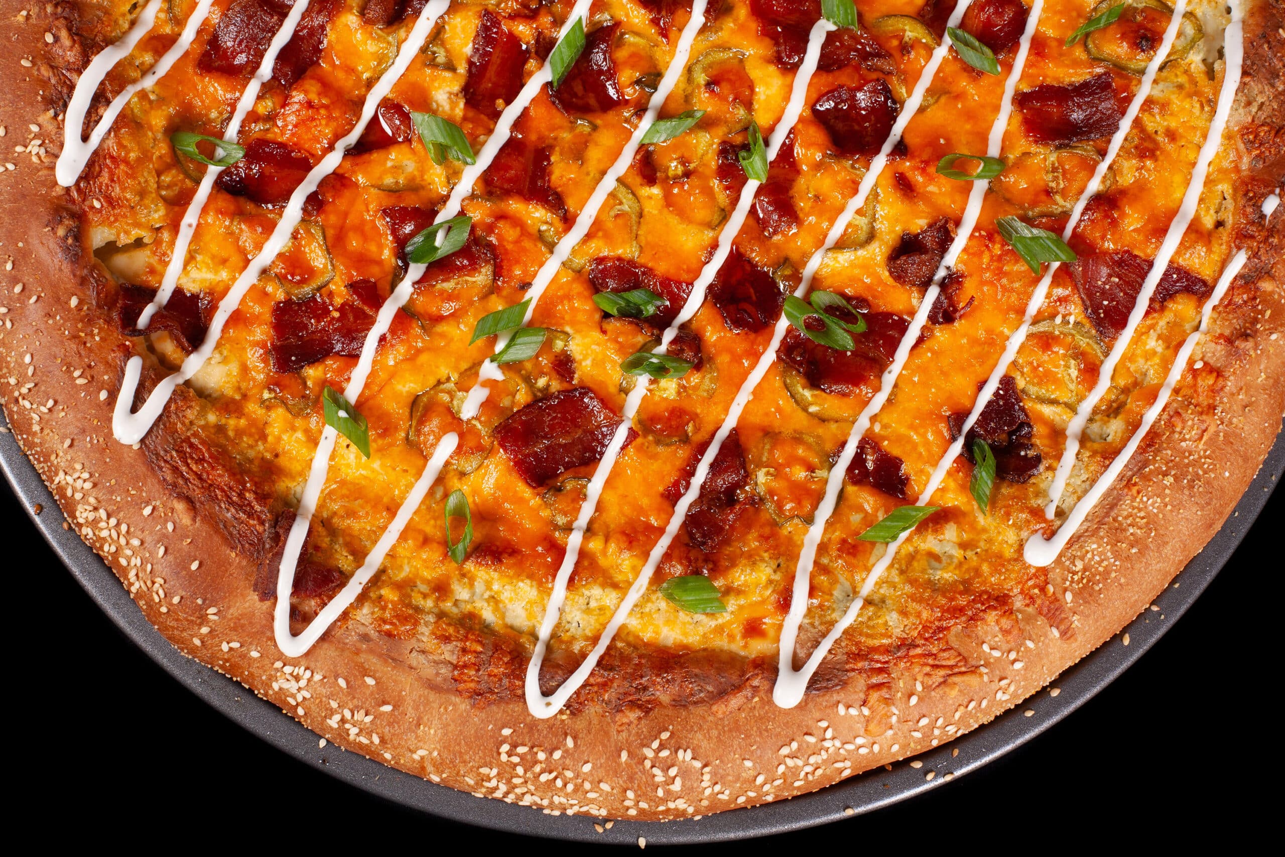 A bacon jalapeno popper stuffed crust pizza drizzled with ranch dressing and topped with sliced green onions.