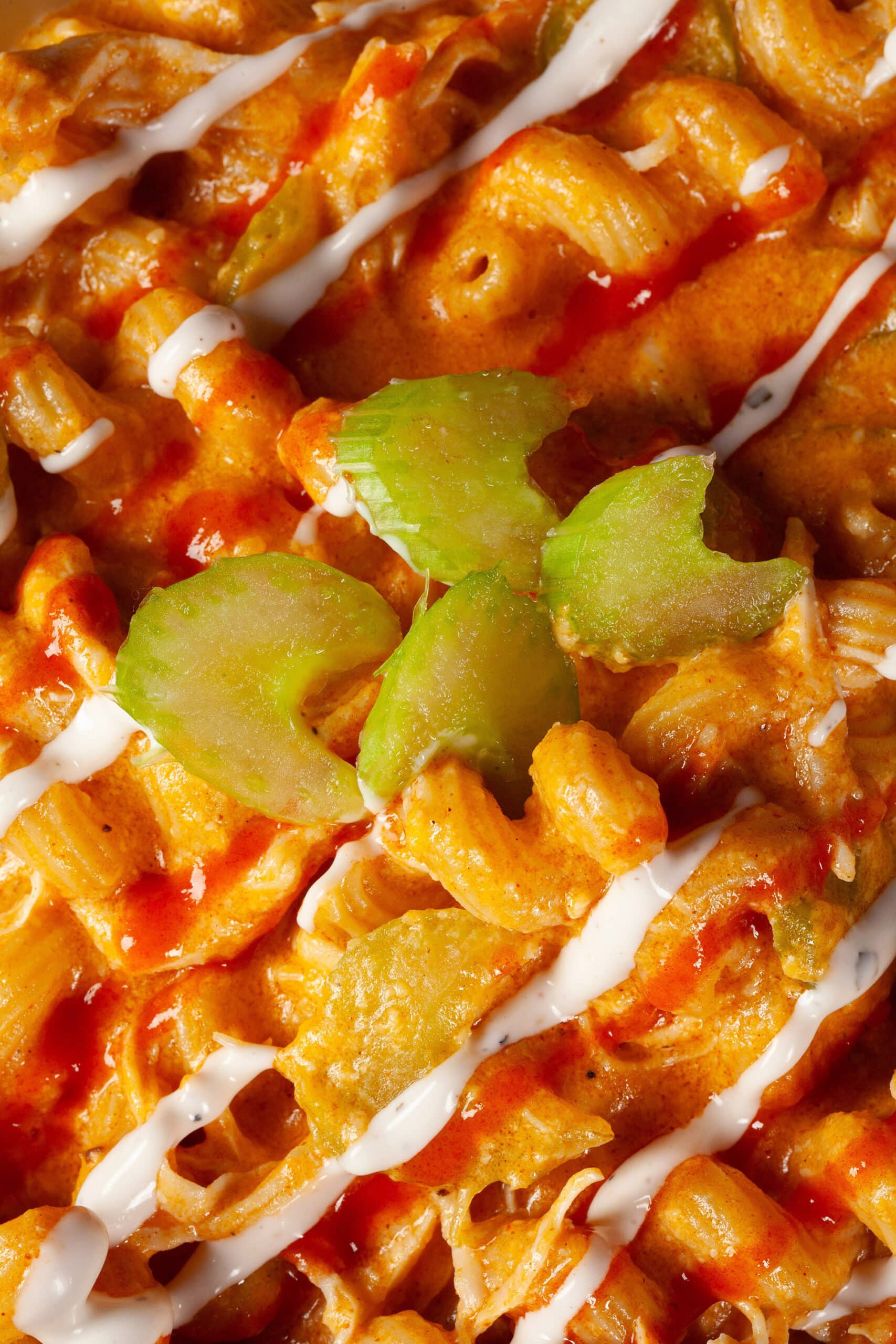 A bowl of buffalo chicken mac and cheese, with spiral pasta, cheese sauce, shredded chicken, celery, and drizzles of ranch dressing and Frank’s redhot sauce.