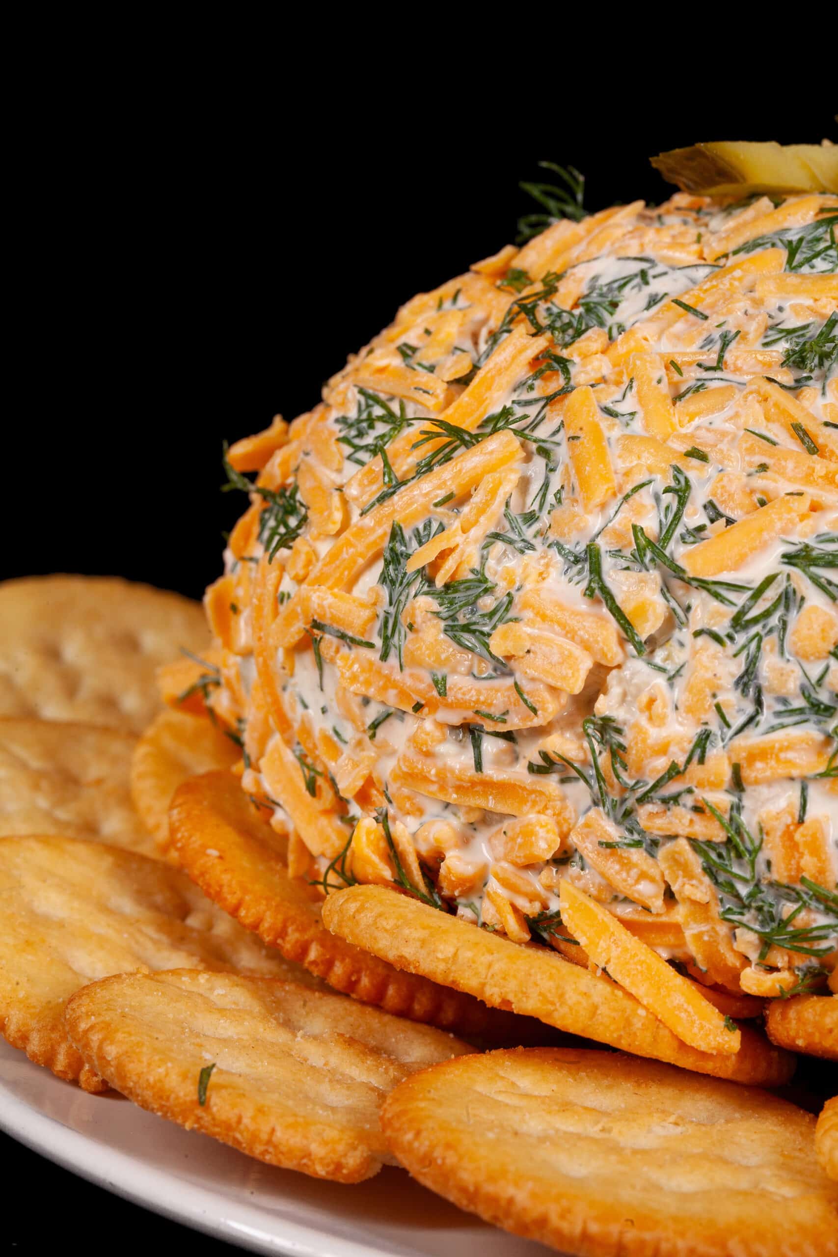 A round, cheese and dill covered dill pickle cheese ball on a plate with Ritz crackers.