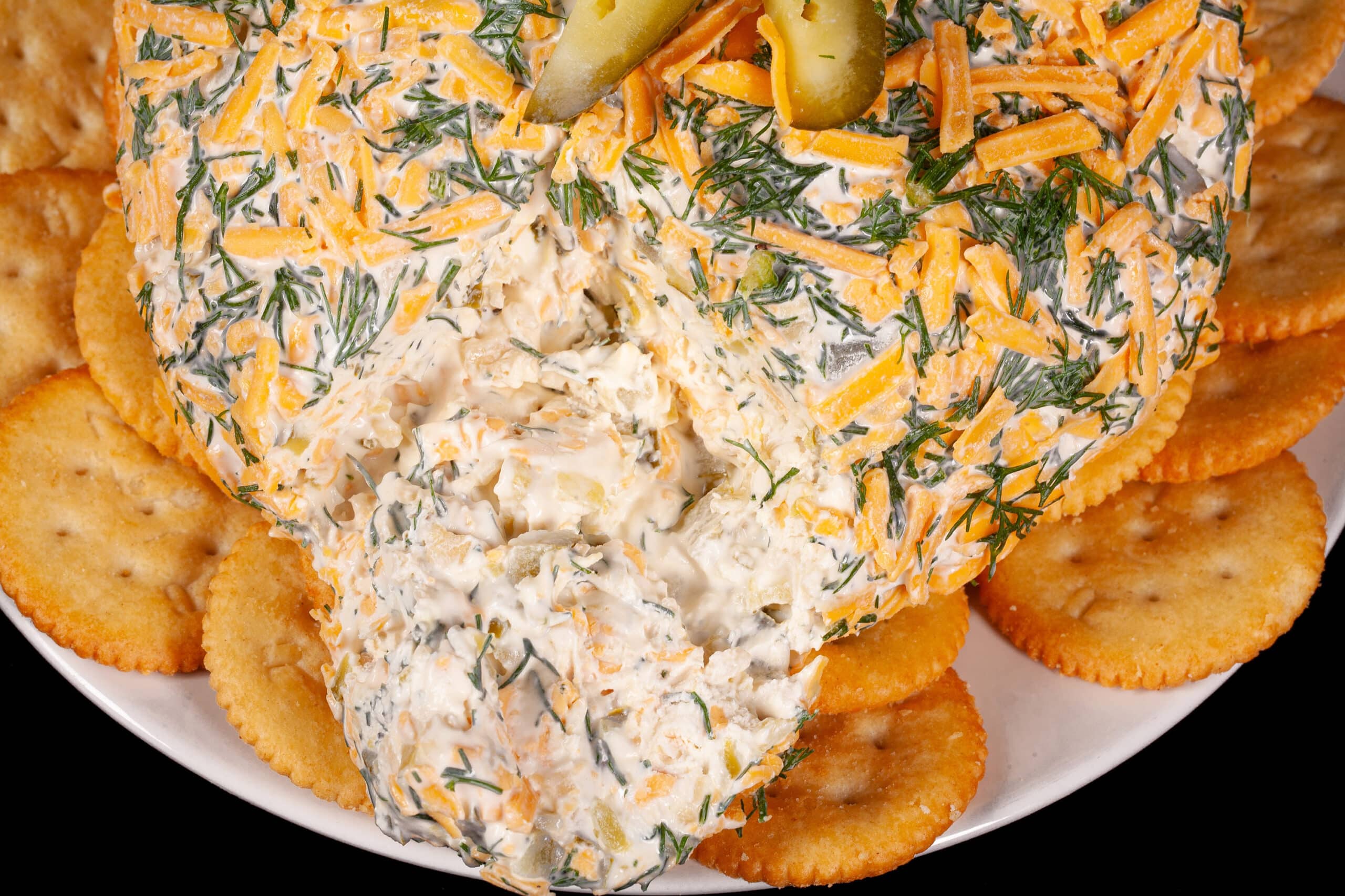 A round, cheese and dill covered dill pickle cheese ball on a plate with Ritz crackers.