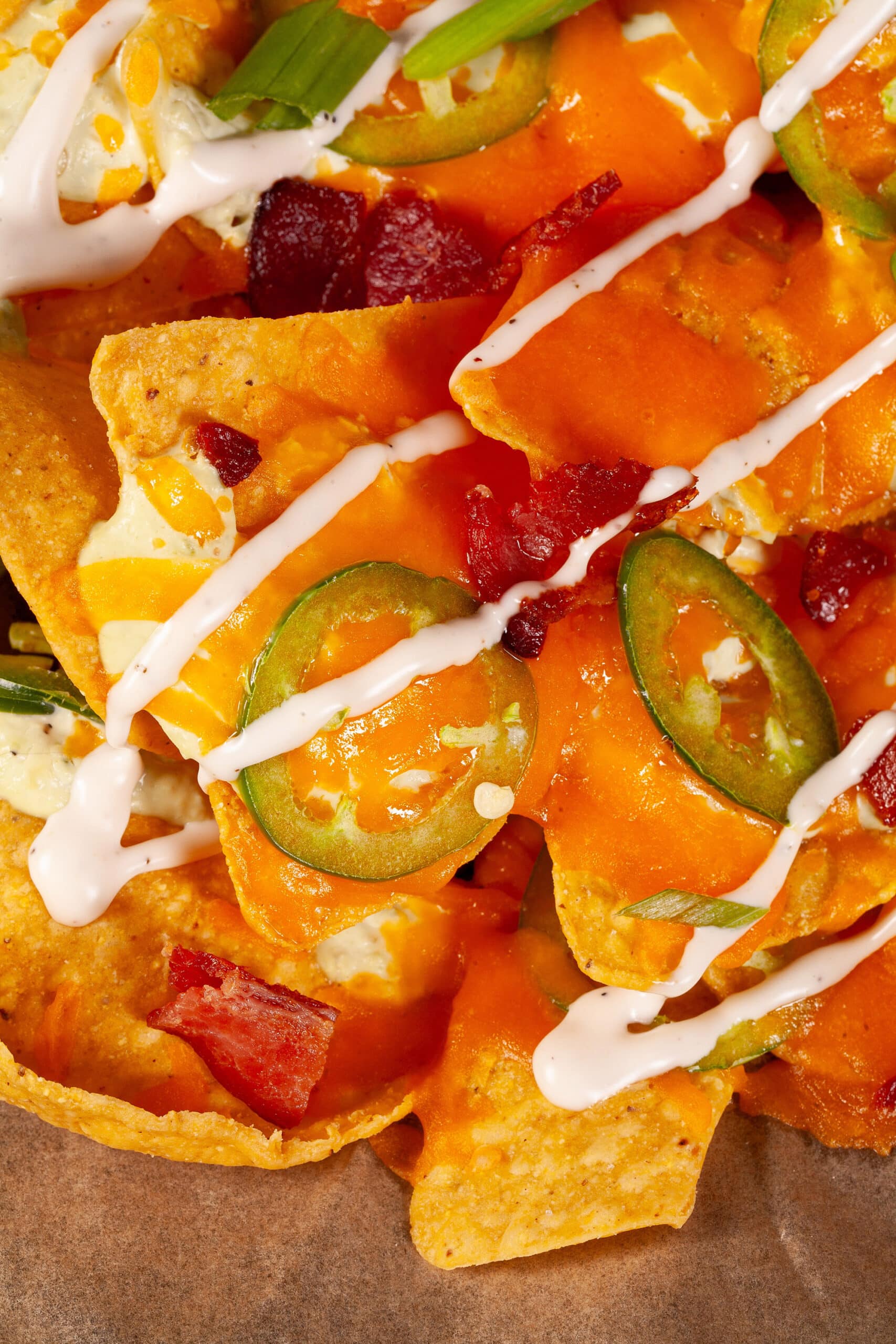 A pan of jalapeno popper nachos with jalapeno cream cheese queso, jalapeno slices, bacon, cheddar, green onions, ranch dressing, and ranch flavoured sour cream.