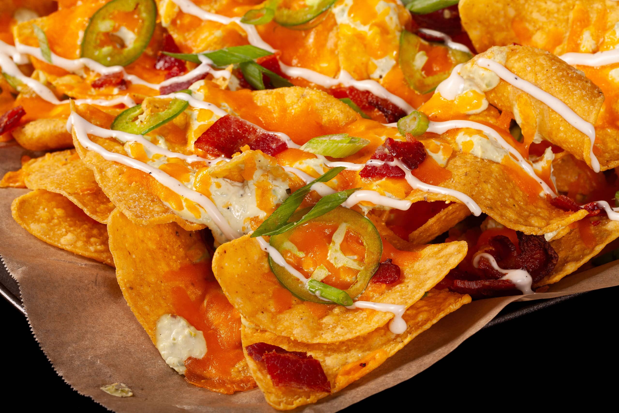 A pan of jalapeno popper nachos with jalapeno cream cheese queso, jalapeno slices, bacon, cheddar, green onions, ranch dressing, and ranch flavoured sour cream.