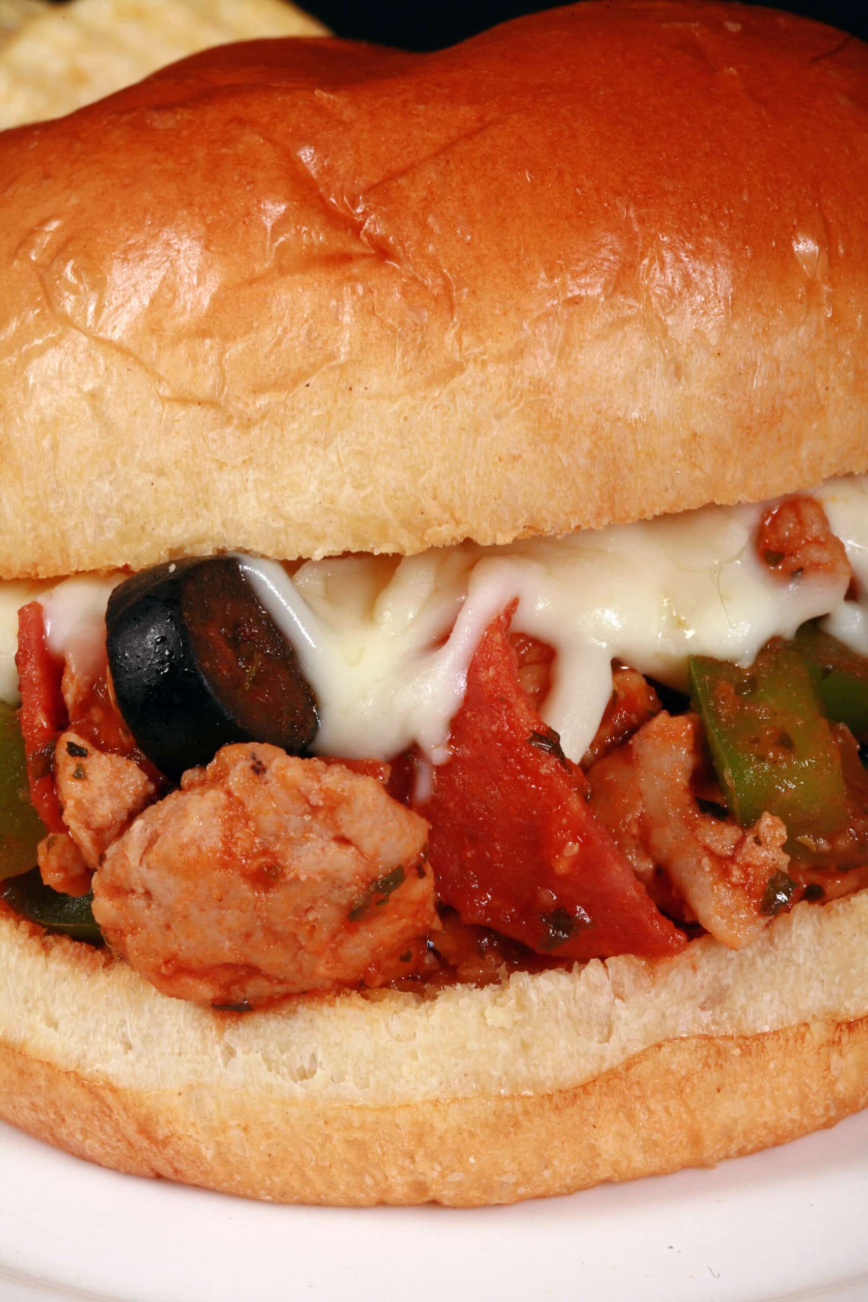 A pizza sloppy joes sandwich on a plate with chips, with pepperoni, green pepper, black olives, and mozzarella cheese visible.