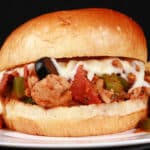 A pizza themed sloppy joes sandwich on a plate with chips, with pepperoni, green pepper, black olives, and mozzarella cheese visible.