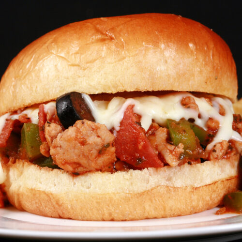 A pizza themed sloppy joes sandwich on a plate with chips, with pepperoni, green pepper, black olives, and mozzarella cheese visible.