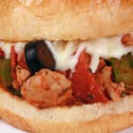 A pizza sloppy joes sandwich on a plate with chips, with pepperoni, green pepper, black olives, and mozzarella cheese visible.