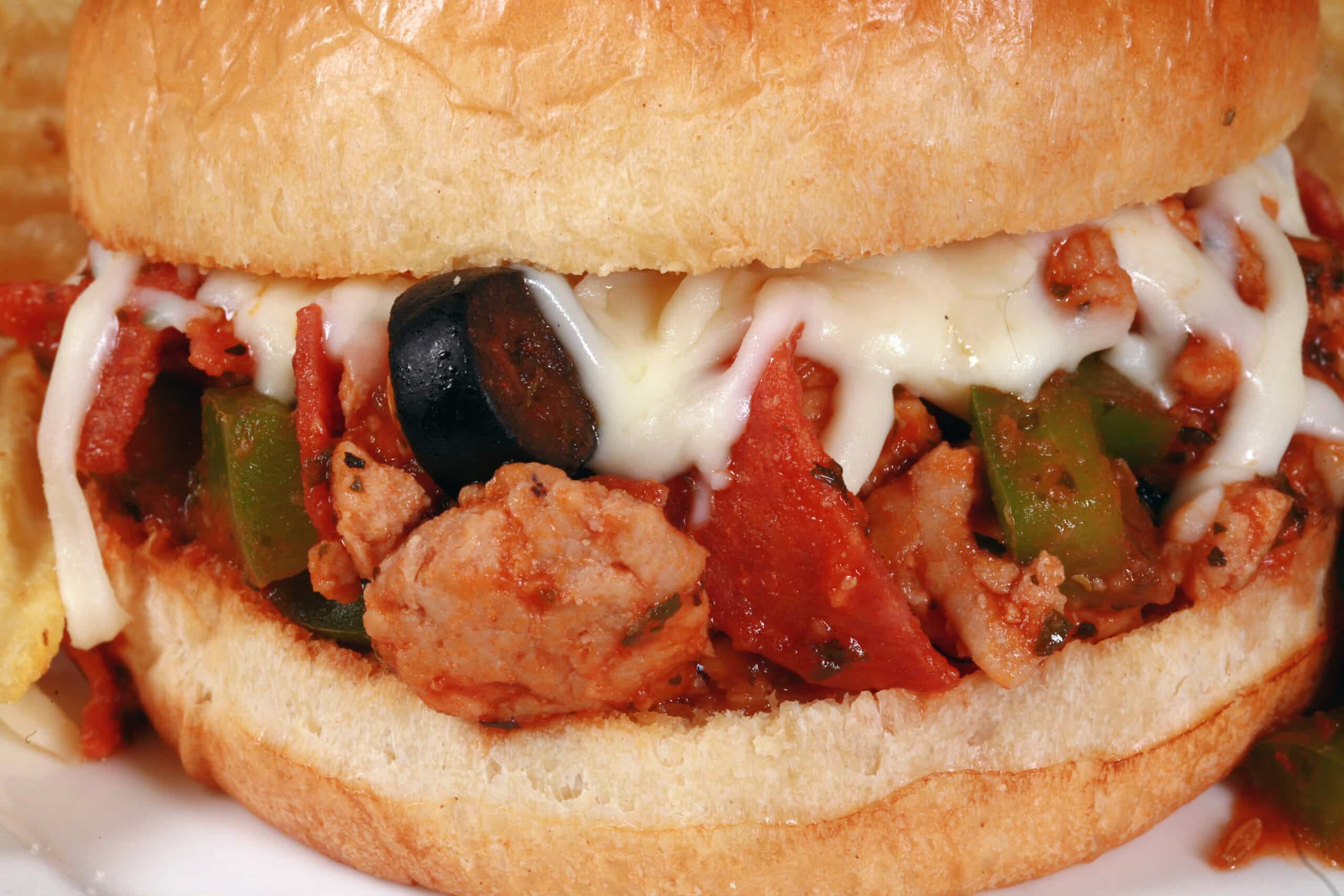 A pizza sloppy joes sandwich on a plate with chips, with pepperoni, green pepper, black olives, and mozzarella cheese visible.