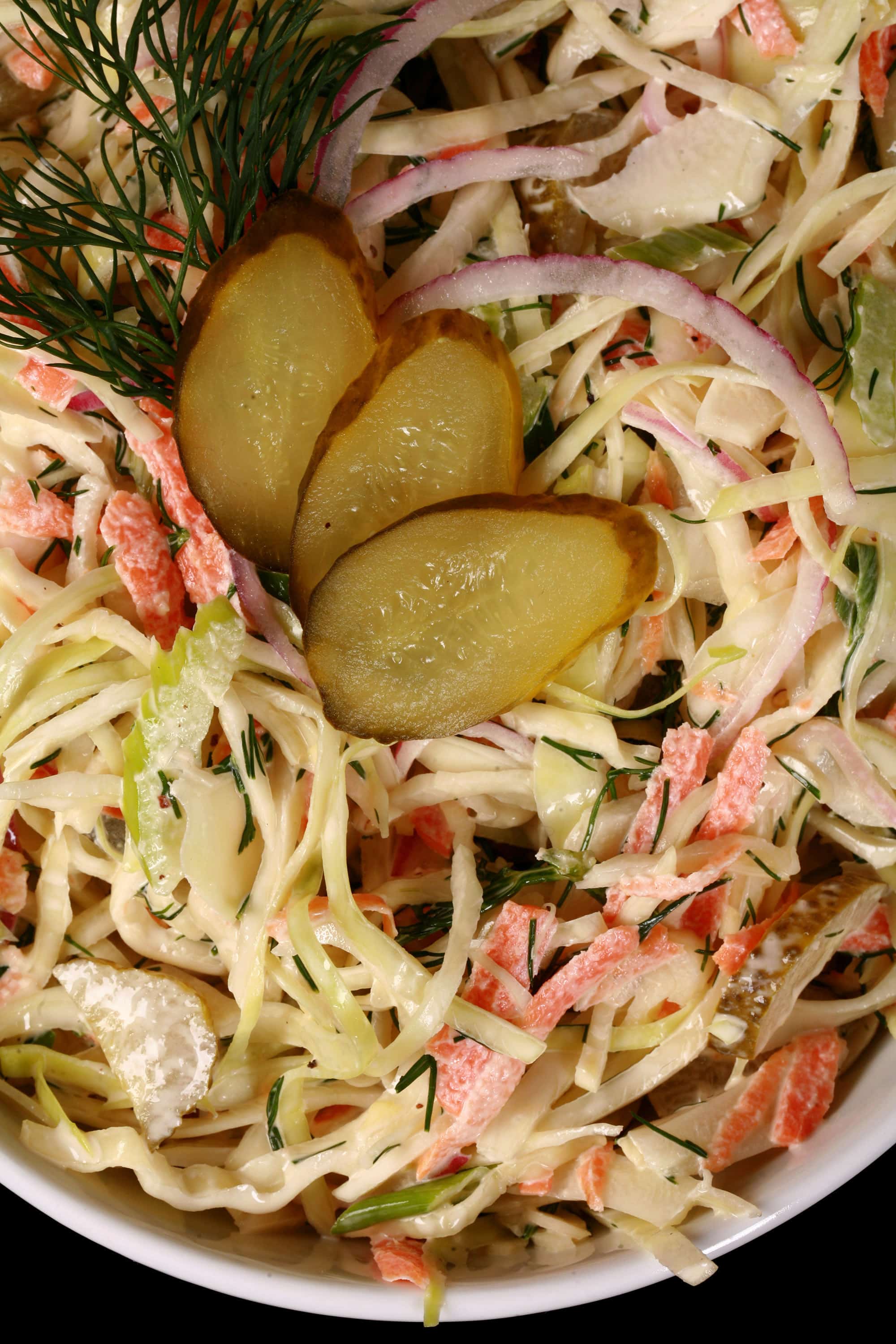 A bowl of creamy dill pickle coleslaw with cabbage, carrots, red onions, pickles, and more.