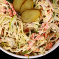 A bowl of creamy dill pickle coleslaw with cabbage, carrots, red onions, pickles, and more.