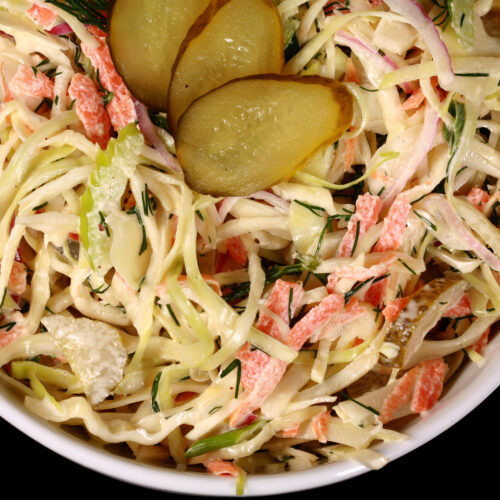 A bowl of creamy dill pickle coleslaw with cabbage, carrots, red onions, pickles, and more.