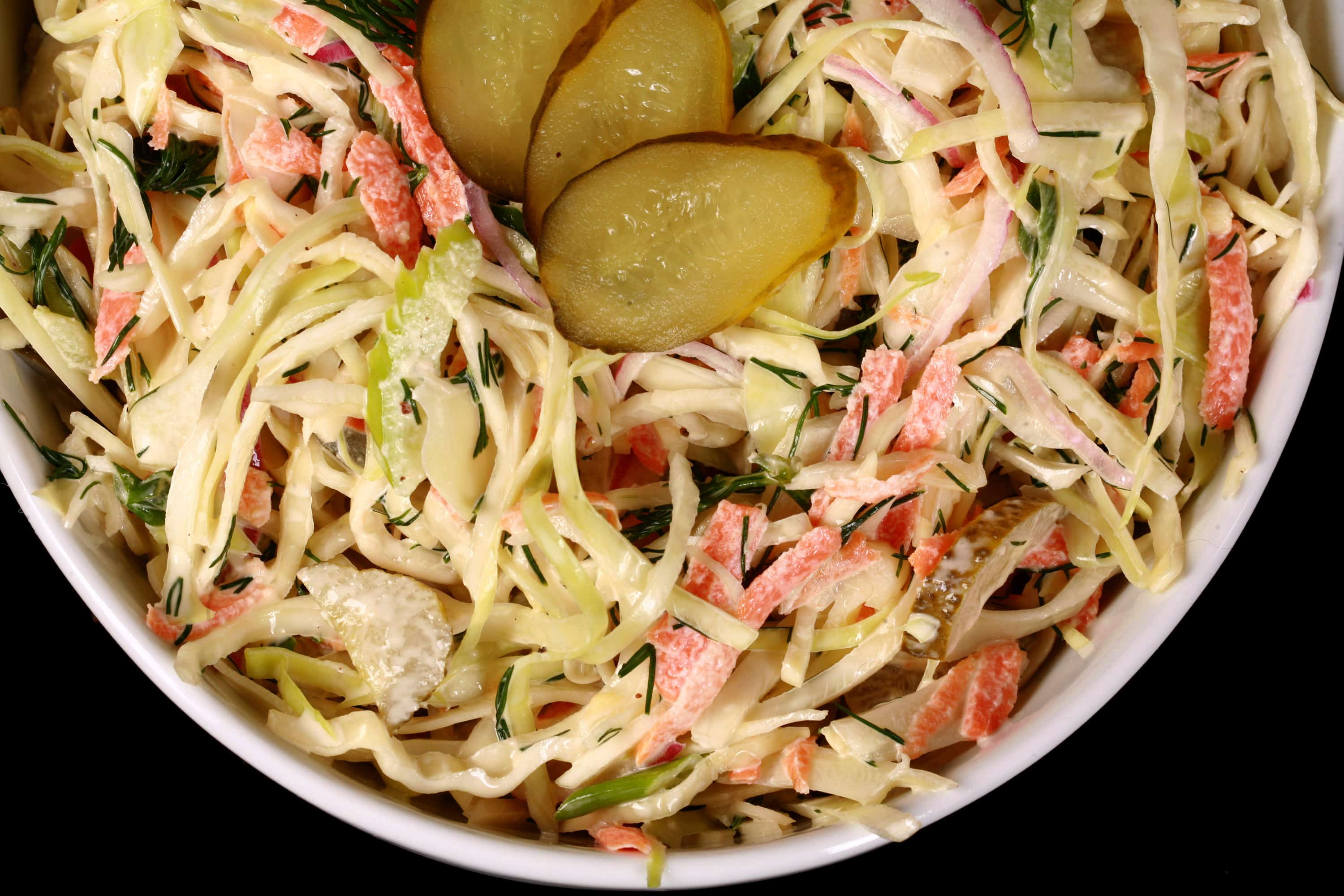 A bowl of creamy dill pickle coleslaw with cabbage, carrots, red onions, pickles, and more.