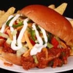 A Taco themed sloppy joe sandwich, with taco meat, lettuce, cheese, salsa, sour cream, and jalapeno slices, on a plate with tortilla chips.