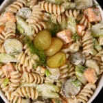 A bowl of dill pickle pasta salad, with slices of pickles, green onion, and celery, fresh dill, and cubes of cheese in a creamy sauce.