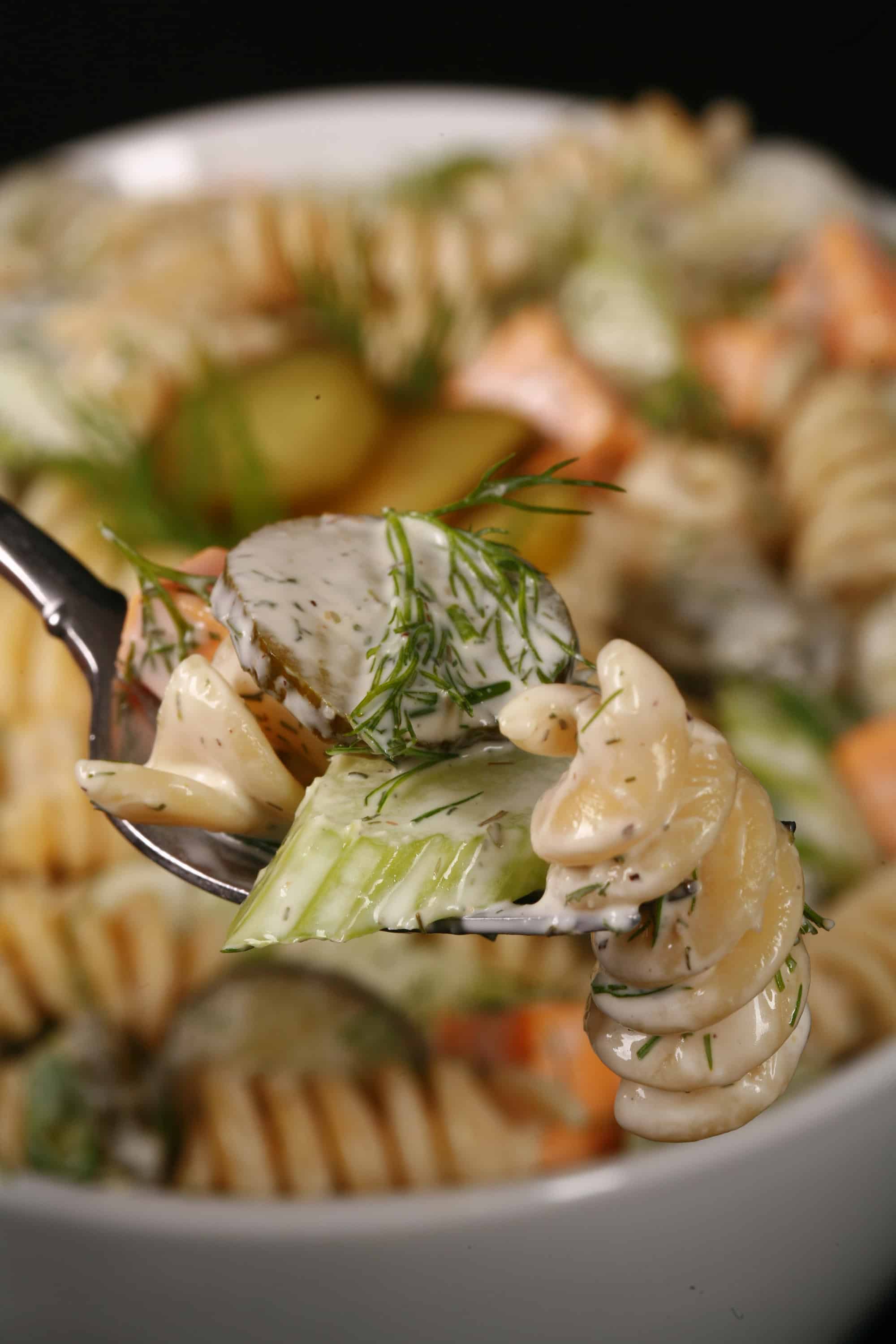 A bowl of dill pickle pasta salad, with slices of pickles, green onion, and celery, fresh dill, and cubes of cheese in a creamy sauce.