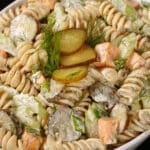 A bowl of dill pickle macaroni salad, with slices of pickles, green onion, and celery, fresh dill, and cubes of cheese in a creamy sauce.