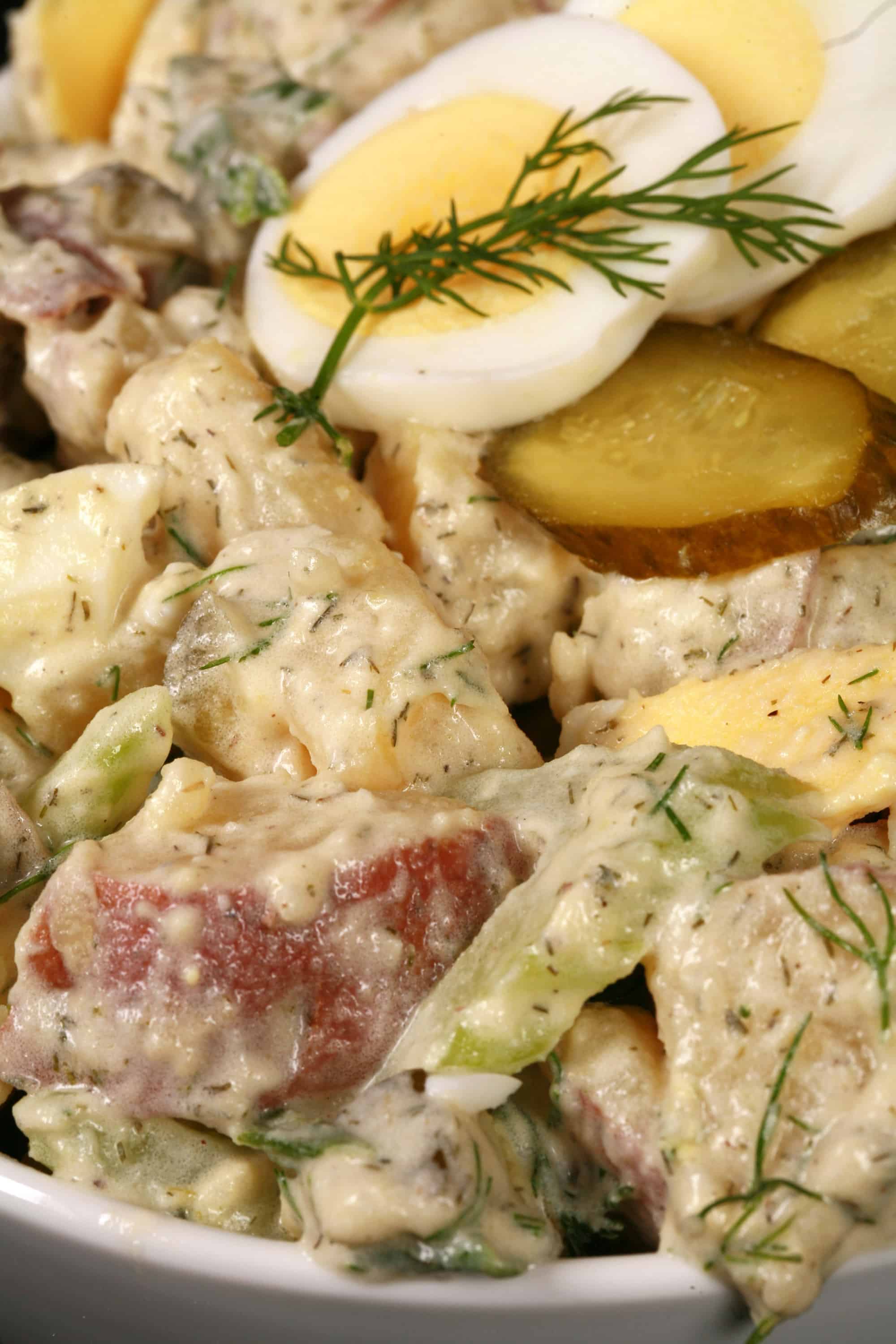A serving bowl of dill pickle potato salad with pickles, boiled eggs, celery, and dill.