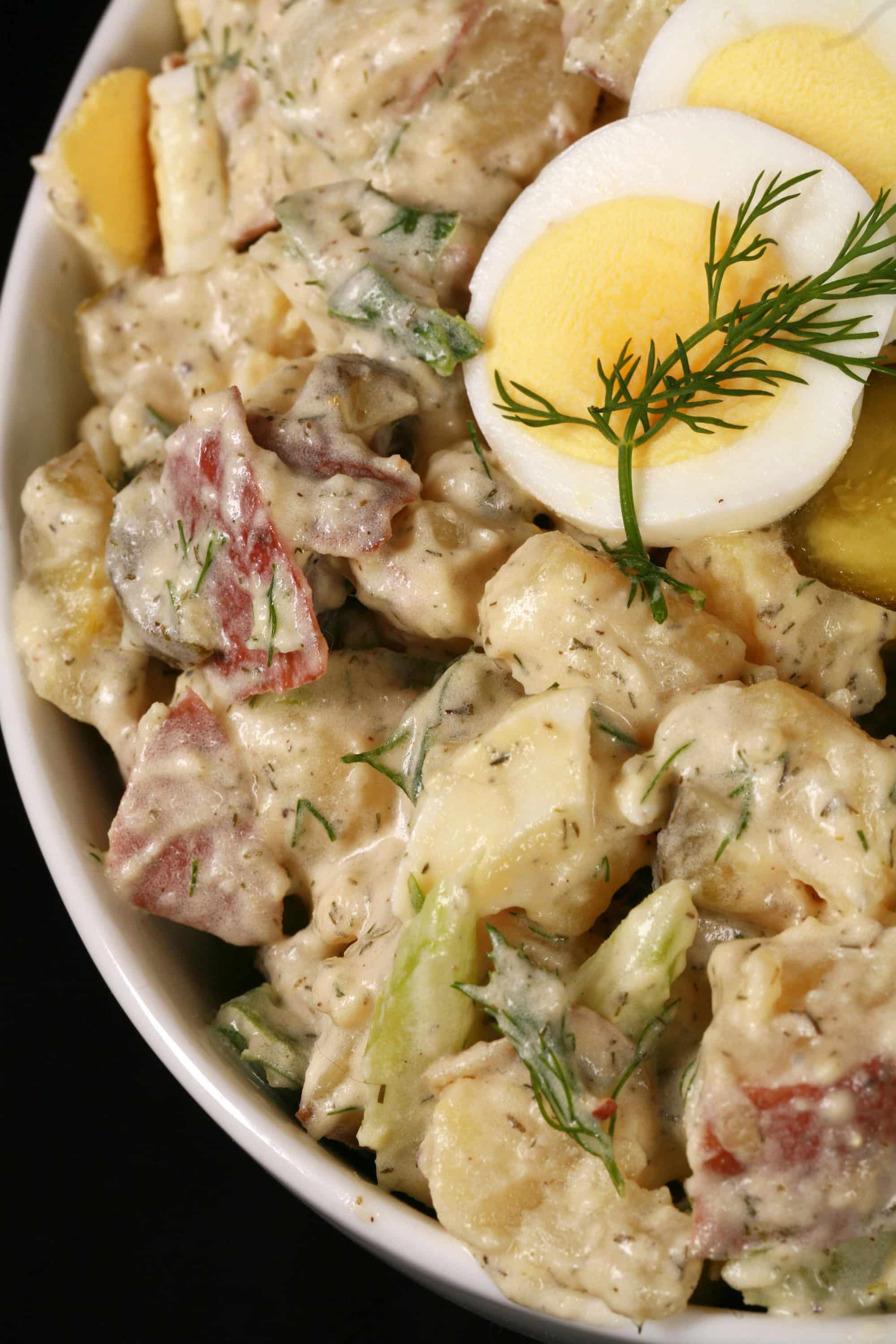 A serving bowl of dill pickle potato salad with pickles, boiled eggs, celery, and dill.