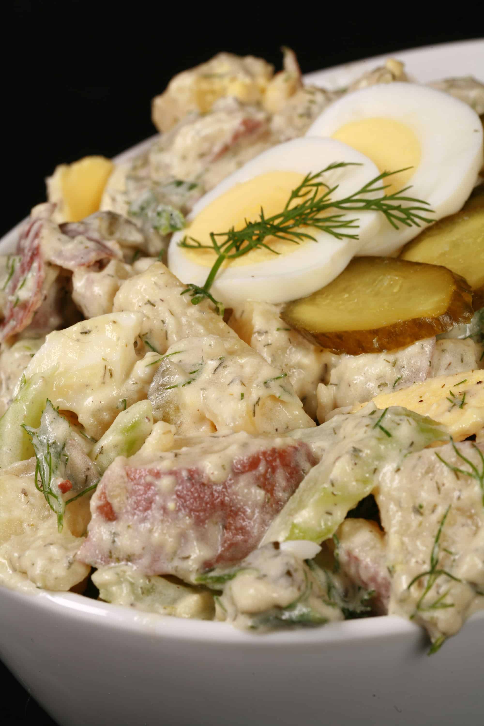 A serving bowl of dill pickle potato salad with pickles, boiled eggs, celery, and dill.
