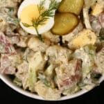 A serving bowl of potato salad with pickles, boiled eggs, celery, and dill.