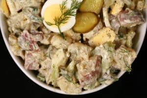 A serving bowl of potato salad with pickles, boiled eggs, celery, and dill.