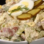 A serving bowl of dill pickle potato salad with pickles, boiled eggs, celery, and dill.