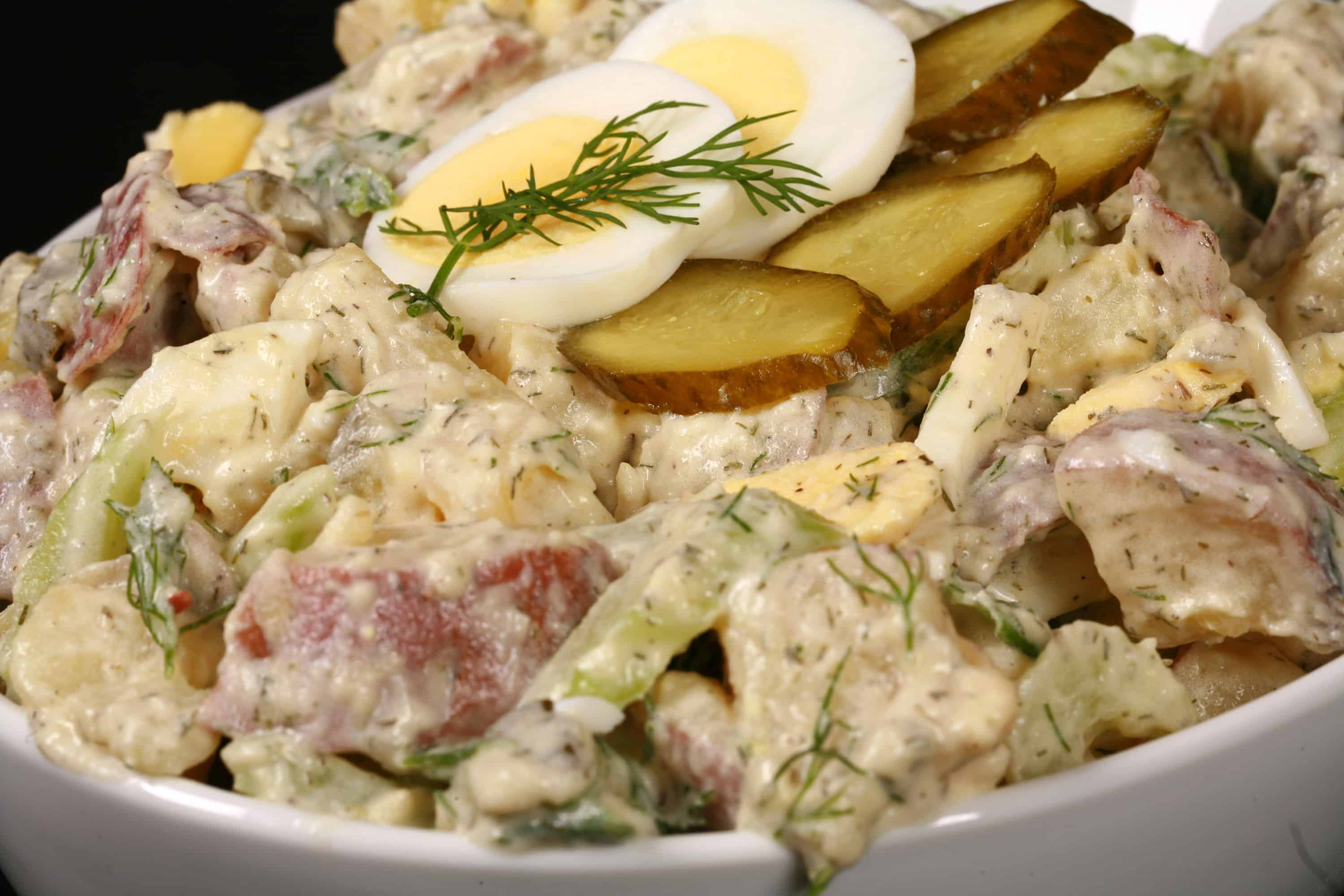 A serving bowl of dill pickle potato salad with pickles, boiled eggs, celery, and dill.