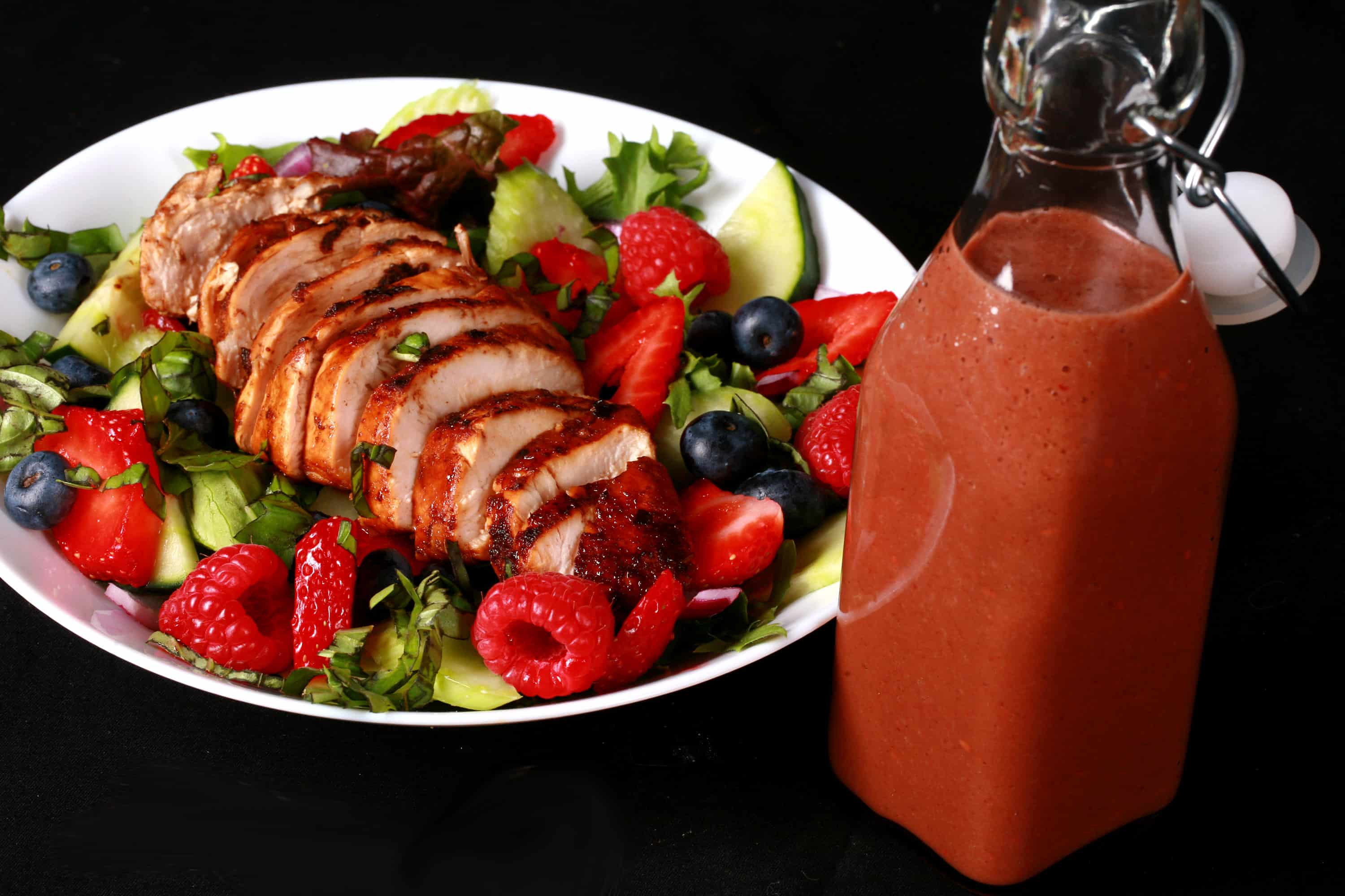 2 summer balsamic salads with balsamic glazed chicken and berries. There is a bottle of fresh raspberry balsamic vinaigrette next to it.