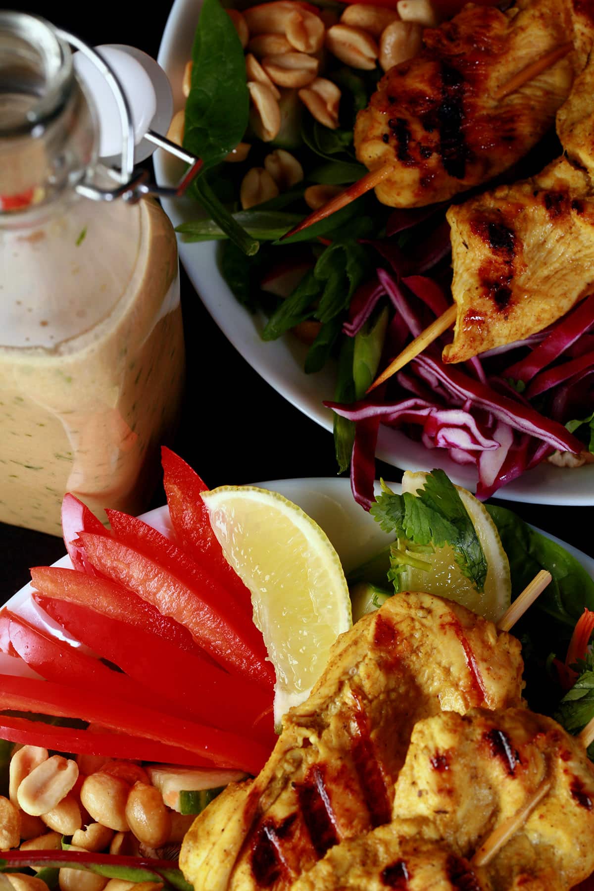 Two grilled chicken satay salads with a bottle of peanut dressing.