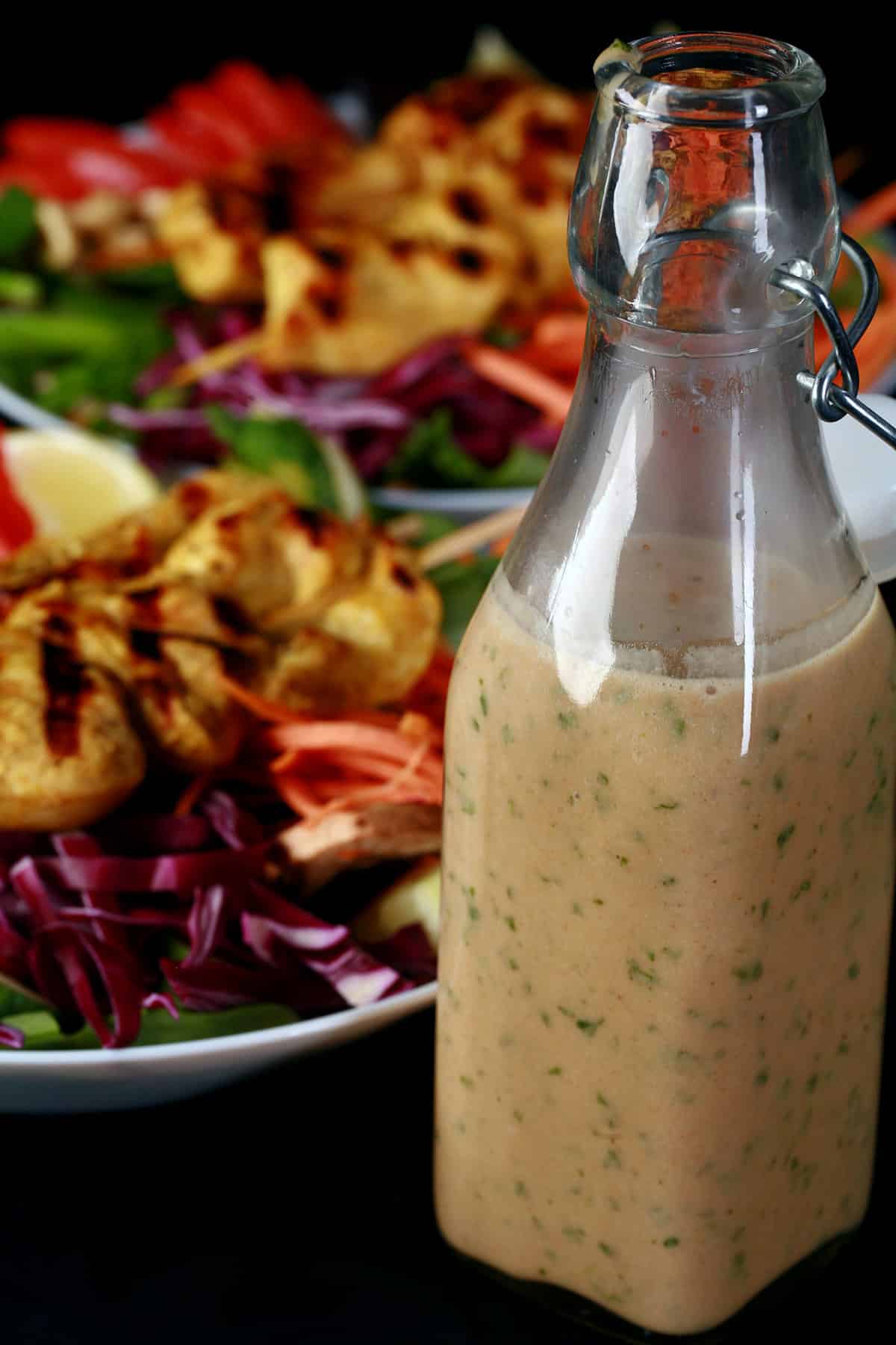 Two grilled chicken satay salads with a bottle of peanut dressing.