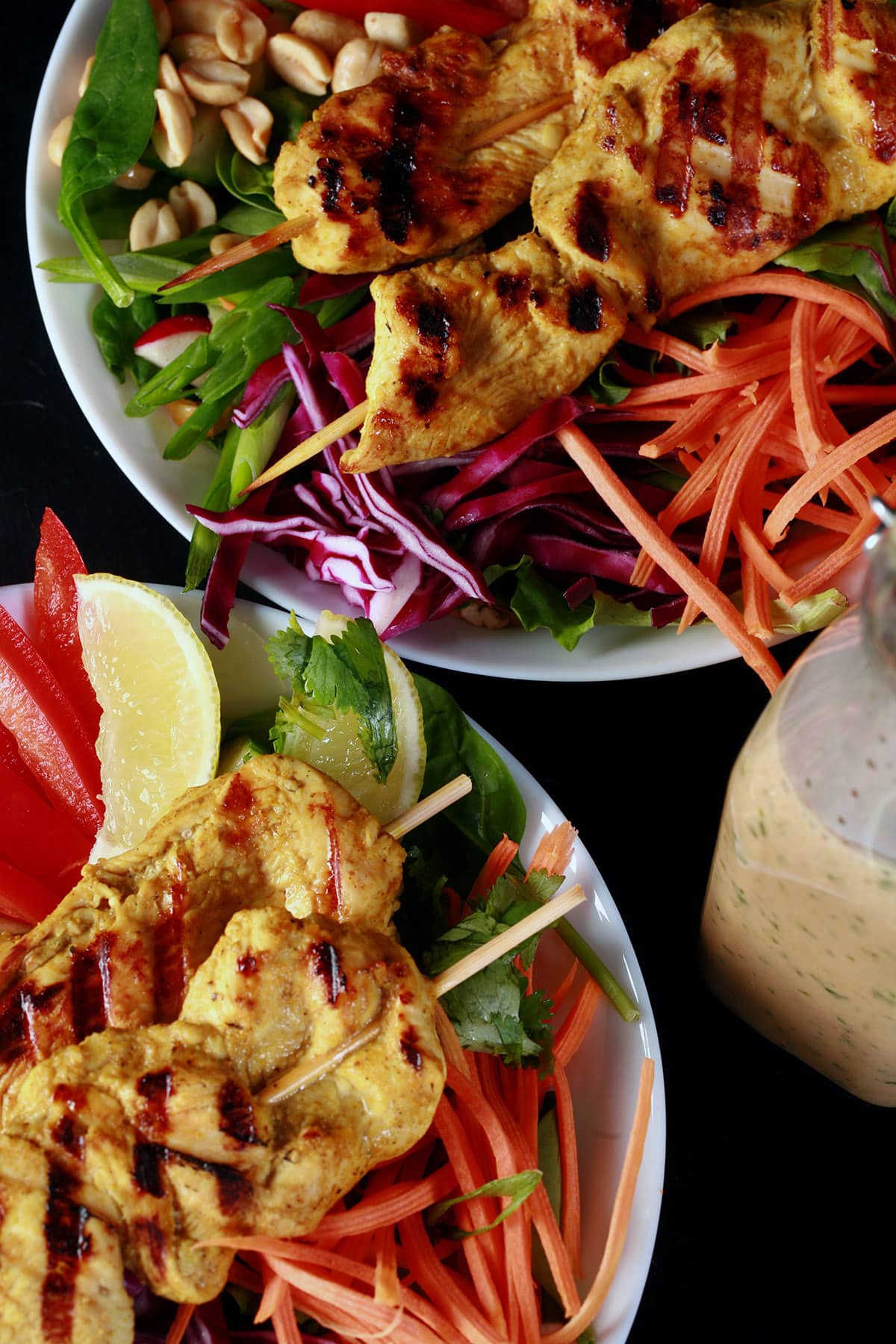 Two grilled chicken satay salads with a bottle of peanut dressing.