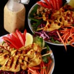 Two grilled chicken satay salads with a bottle of peanut dressing.
