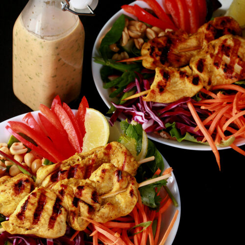 Two grilled chicken satay salads with a bottle of peanut dressing.