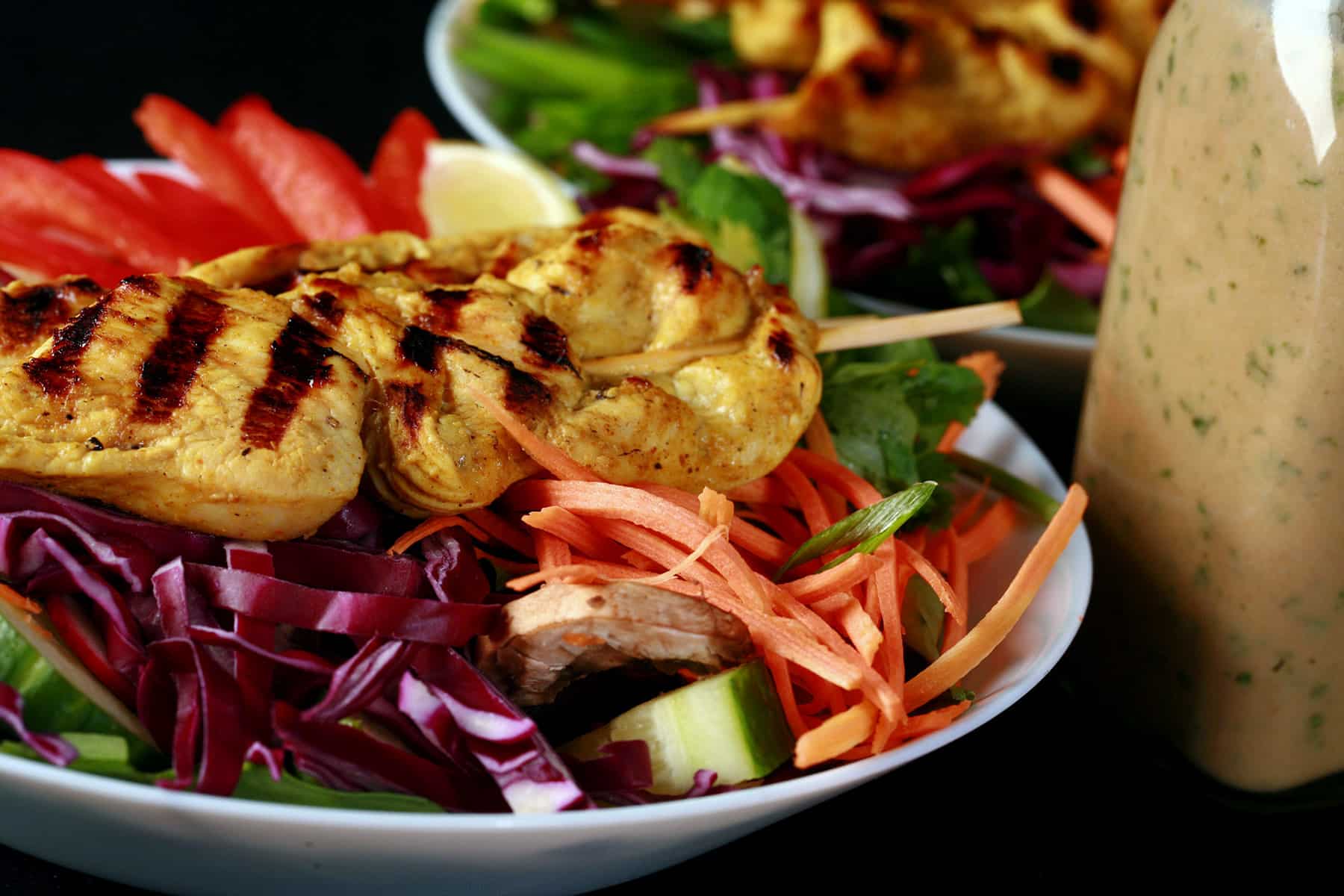 Two grilled chicken satay salads with a bottle of peanut dressing.