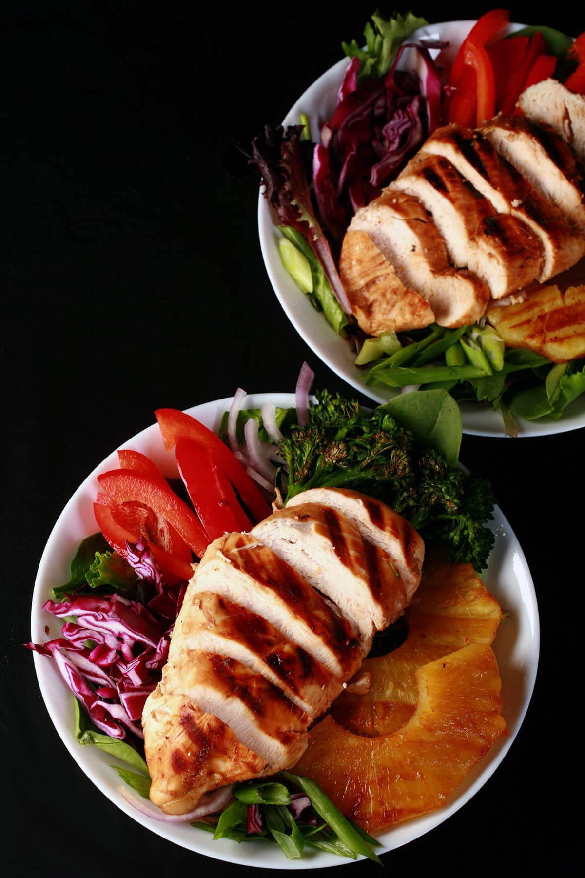 Two grilled chicken teriyaki salads with fresh pineapple.
